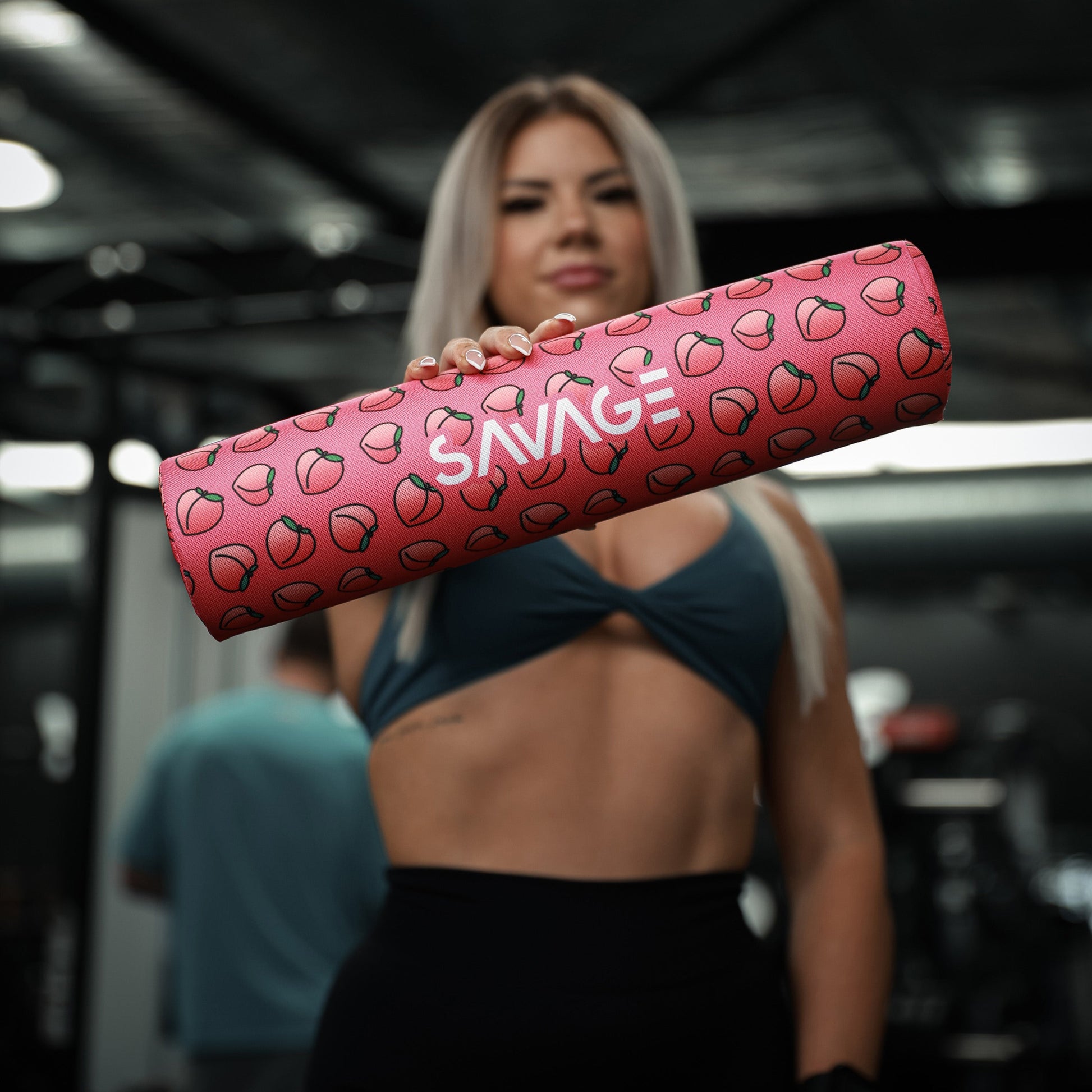 Woman holding a peachy pattern Savage barbell pad in a gym setting