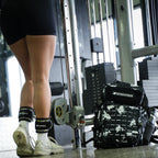 Person in gym wearing black shorts and white sneakers with a camouflage backpack.