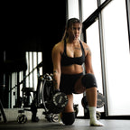 Woman lifting weights in a gym setting doing dumbbell lunges with lifting straps and wearing Savage Fitness  knee sleeves