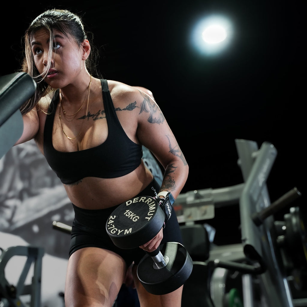 Woman lifting weights in a gym setting doing dumbbell rows with lifting straps