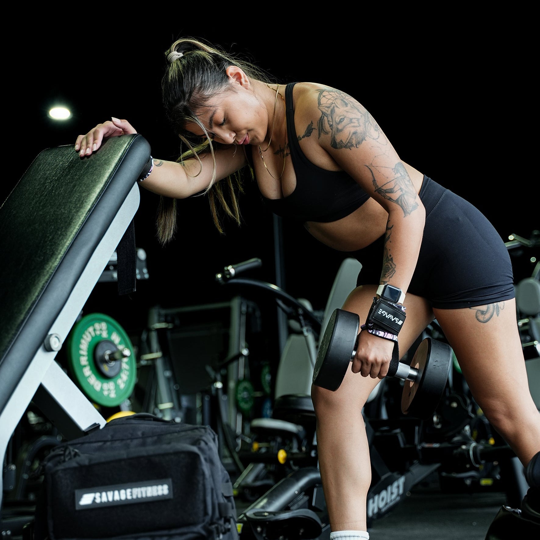 Woman lifting weights in a gym setting doing dumbbell rows with lifting straps