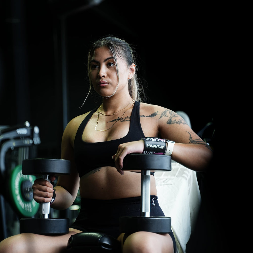 A woman lifting weights in a gym setting. Using Savage Fitness wrist wraps