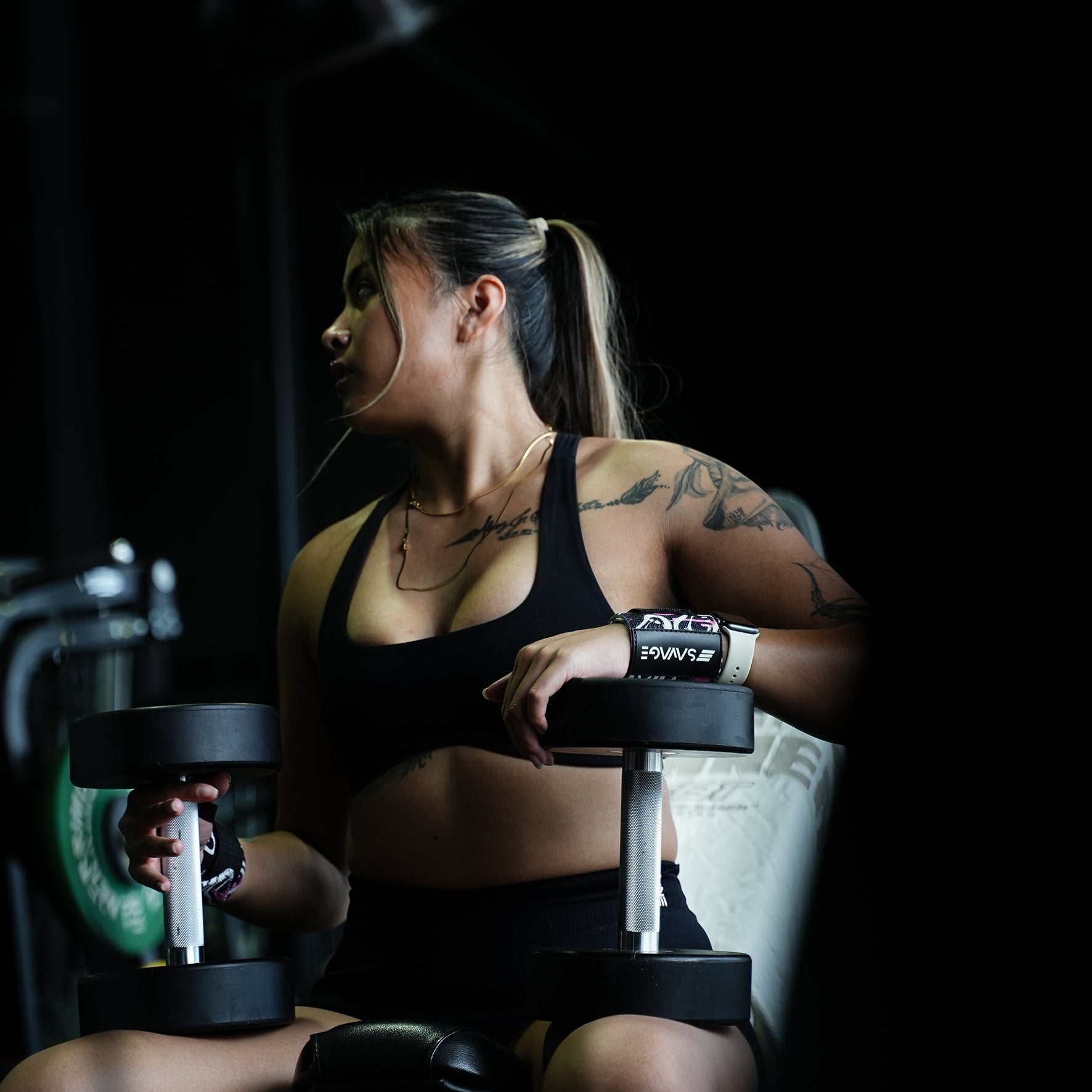 A woman lifting weights in a gym setting. Using Savage Fitness wrist wraps