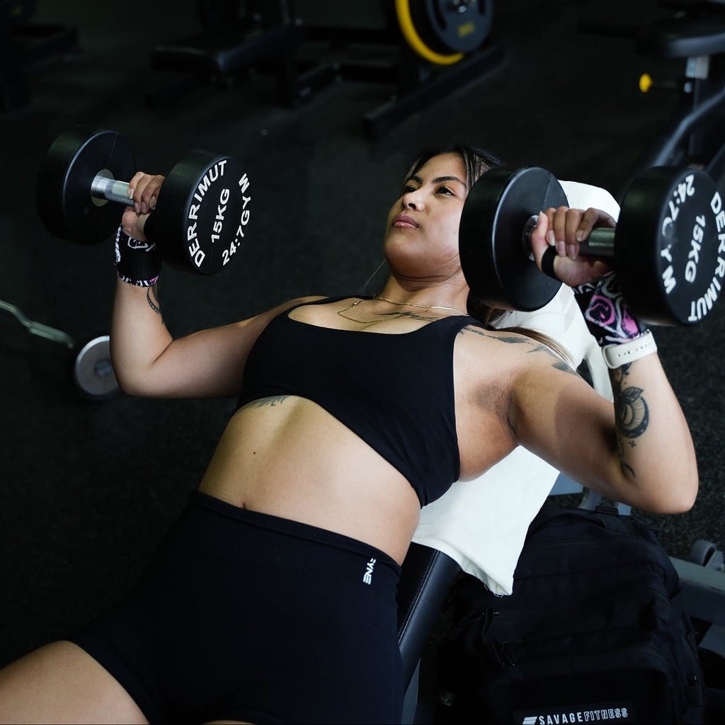 A woman lifting weights in a gym setting. Using Savage Fitness wrist wraps