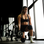Woman in a gym holding dumbbells with large windows in the background
