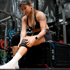Woman sitting on a weight bench in a gym setting putting on Savage Fitness Knee Sleeves