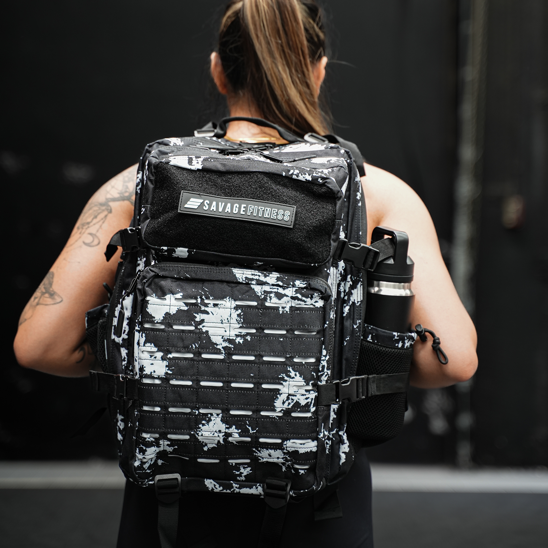 Person wearing a black and white Savage Fitness tactical backpack with 'Savage Fitness' branding. Recon Tactical bag