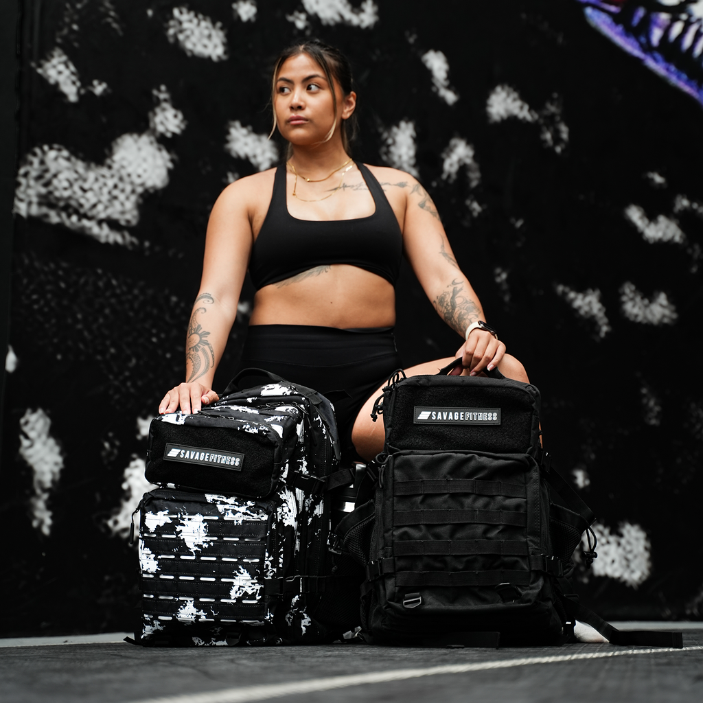 Woman sitting on a basketball court with two Savage Fitness Tactical bags.
