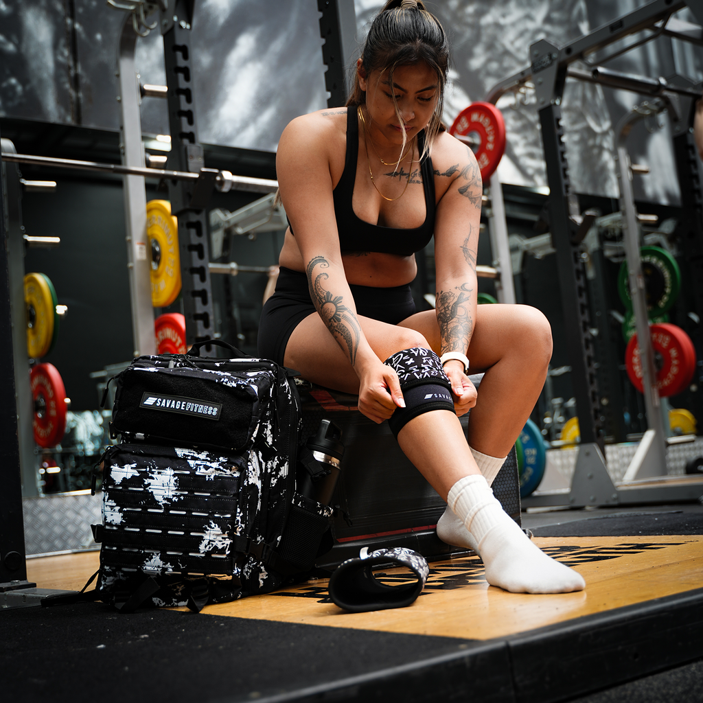 Woman preparing for a workout in a gym setting - putting on Savage Fitness Knee Sleeves