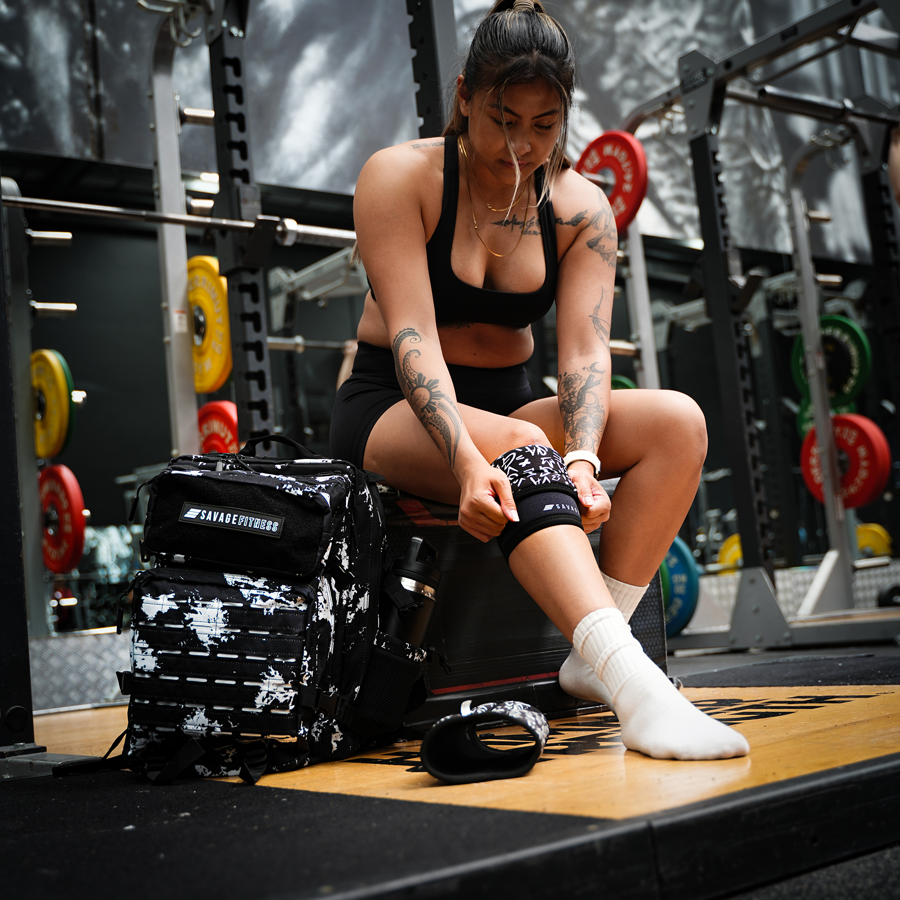Woman preparing for a workout in a gym setting - putting on Savage Fitness Knee Sleeves