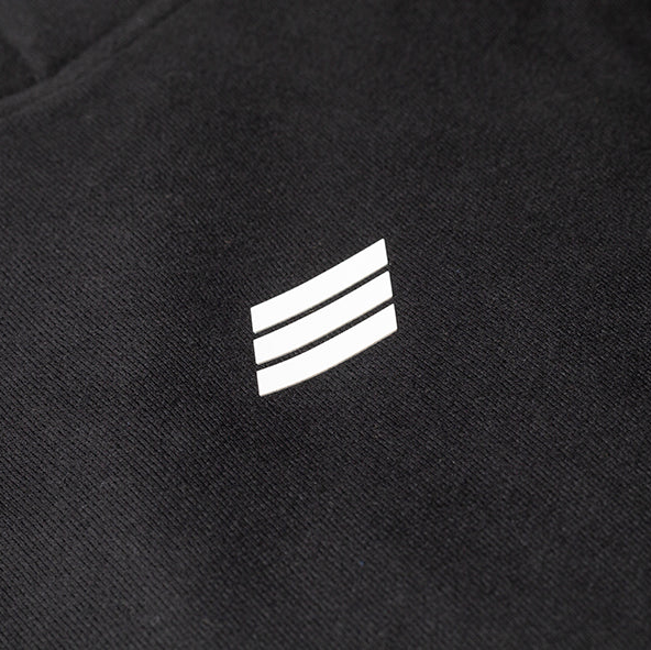 Close-up of a black textured fabric with a small white three-stripe logo centered on the chest.