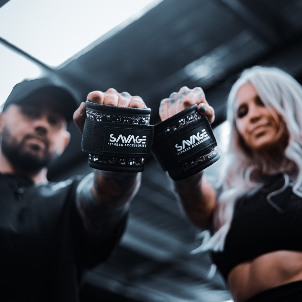 Two people holding black ankle wraps with 'Savage Fitness Accessories' branding in a gym setting.